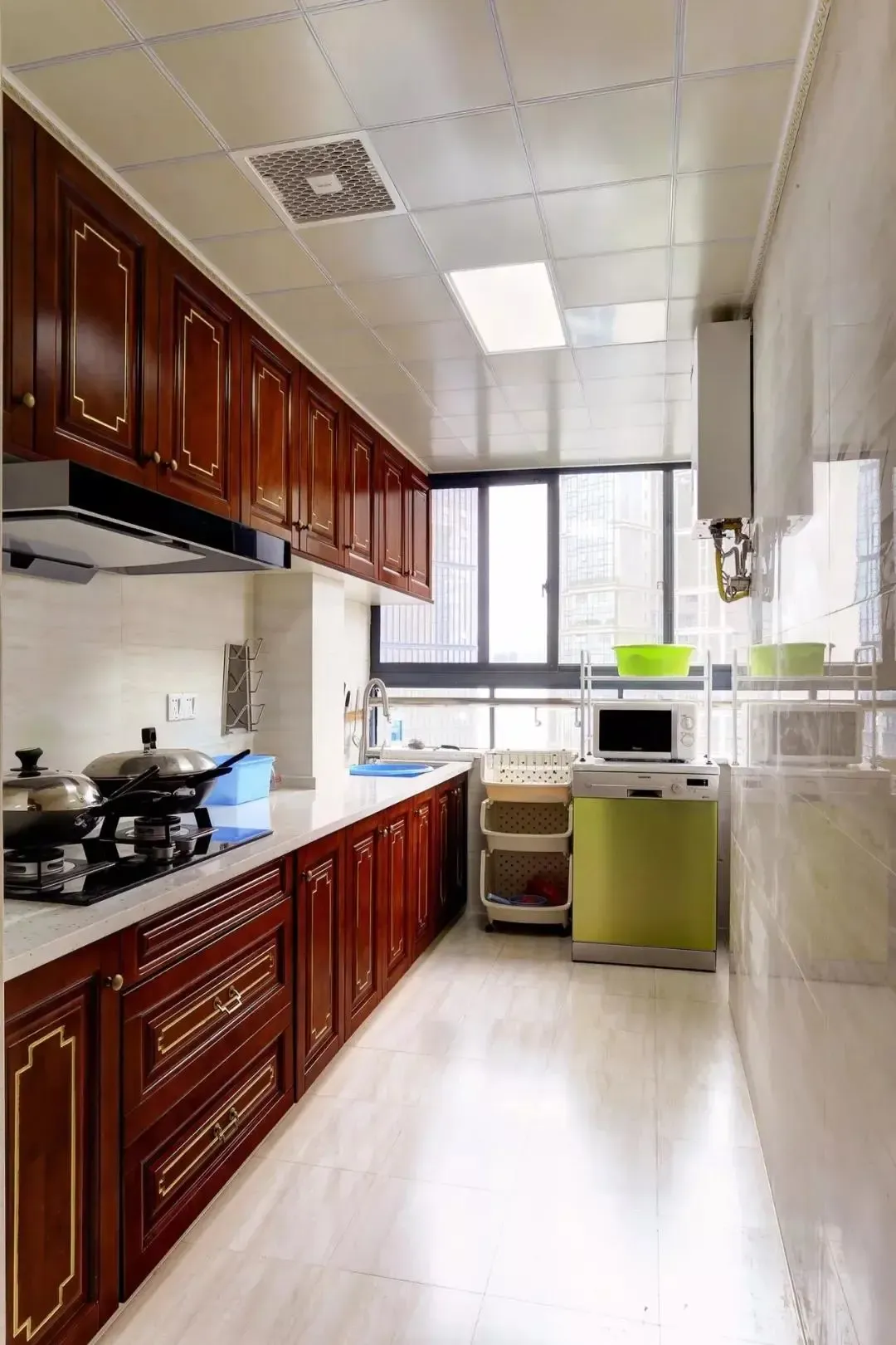 一字型的长条厨房,在靠窗位置还摆着一个移动料理架,而红木质感的橱柜